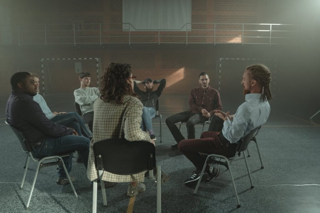 A diverse group engages in a therapy session inside a gym, fostering mental health support.