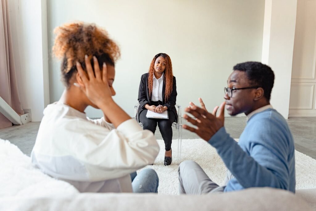 A couple in therapy session with a mental health professional indoors.