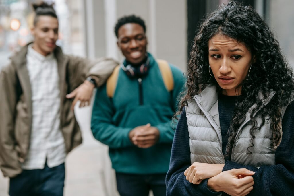 Laughing multiracial teenage boys mocking at depressed young ethnic female standing on street after school